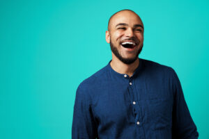 Joyful dark-skinned man laughing against turquoise background close up